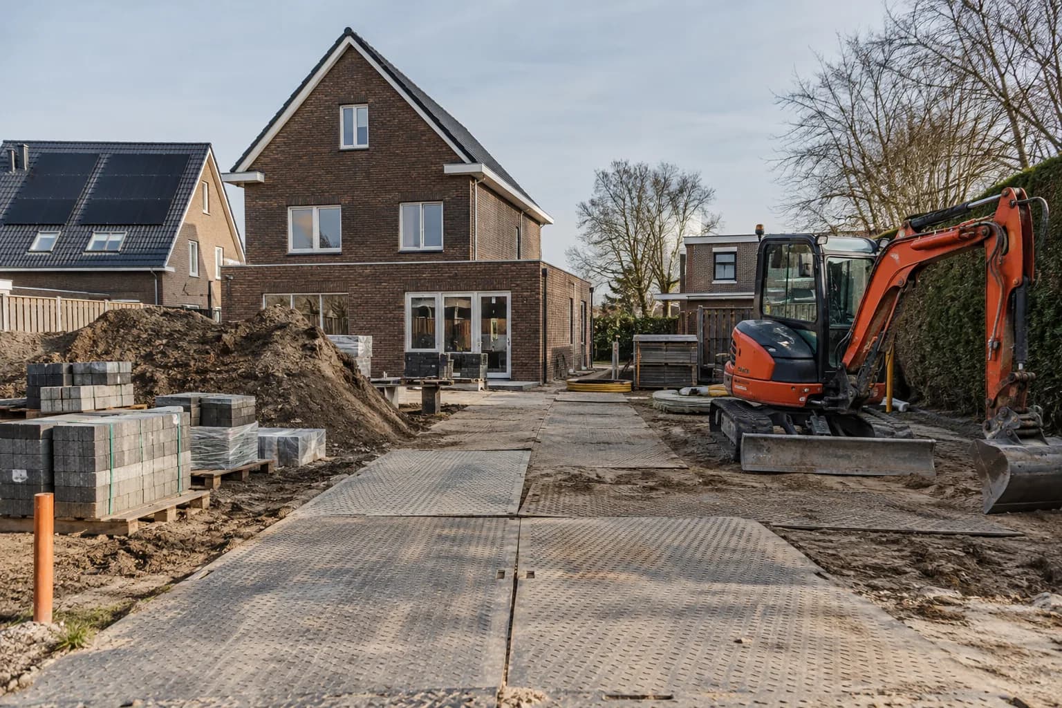 Bouwplaats met rijplaten, gescheiden materiaalopslag en een minigraver