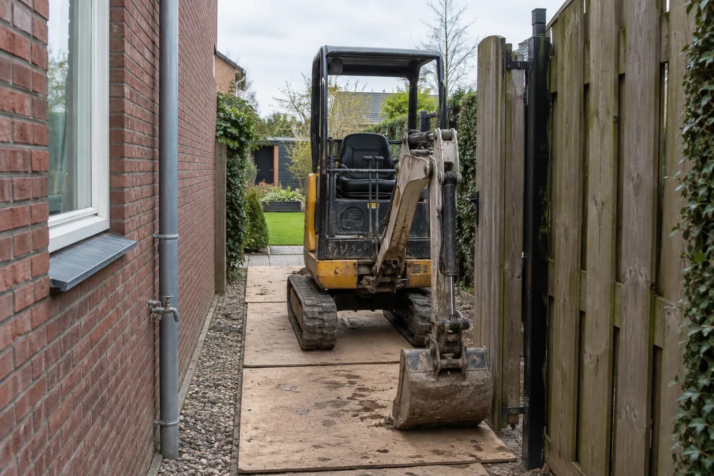 AI-illustratie: Compacte minigraver op rijplaten in een smalle doorgang tussen woning en schutting