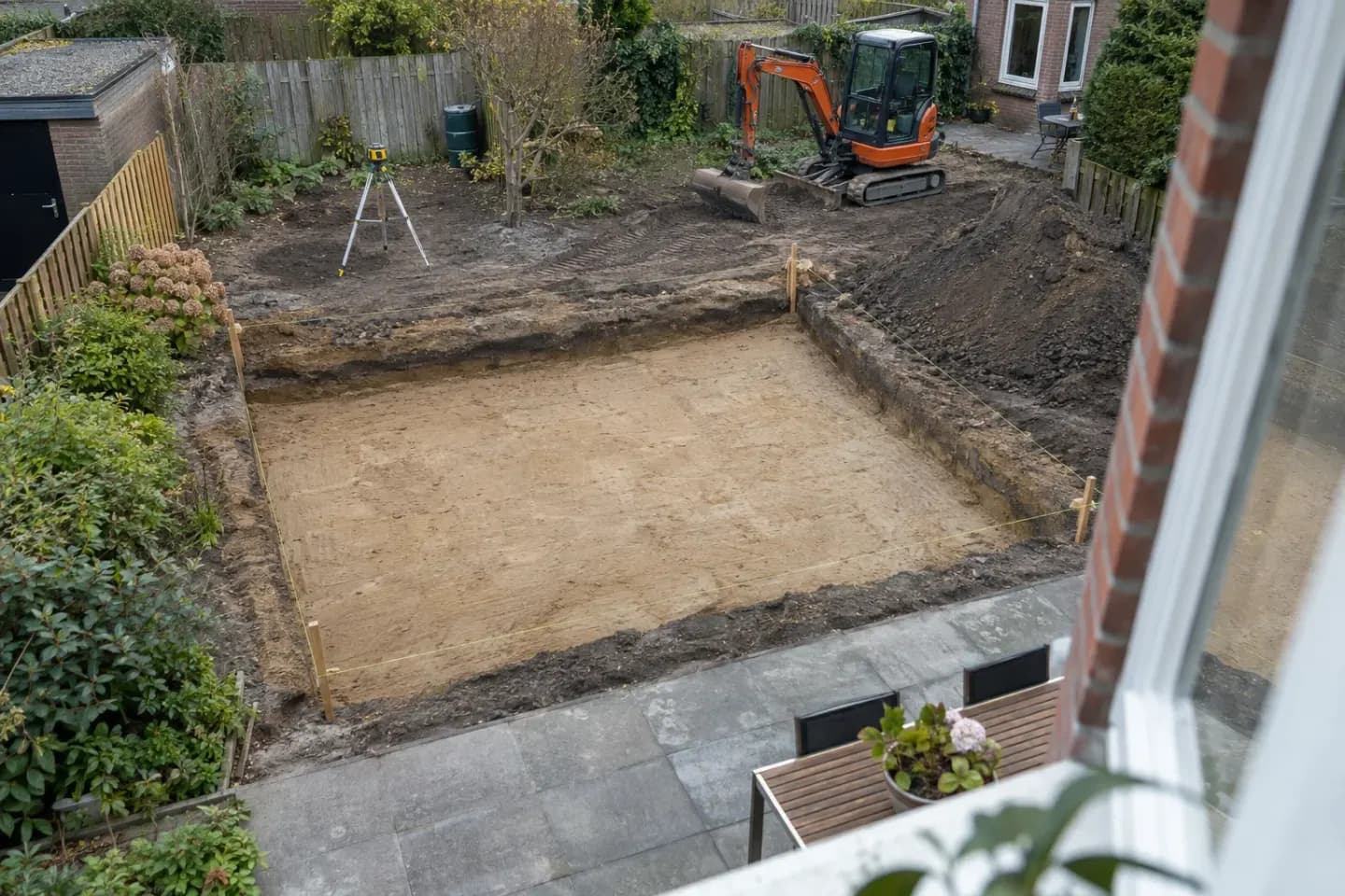 AI-illustratie: Rechthoekige bouwput van bovenaf met uitzetkoord, laser en minigraver