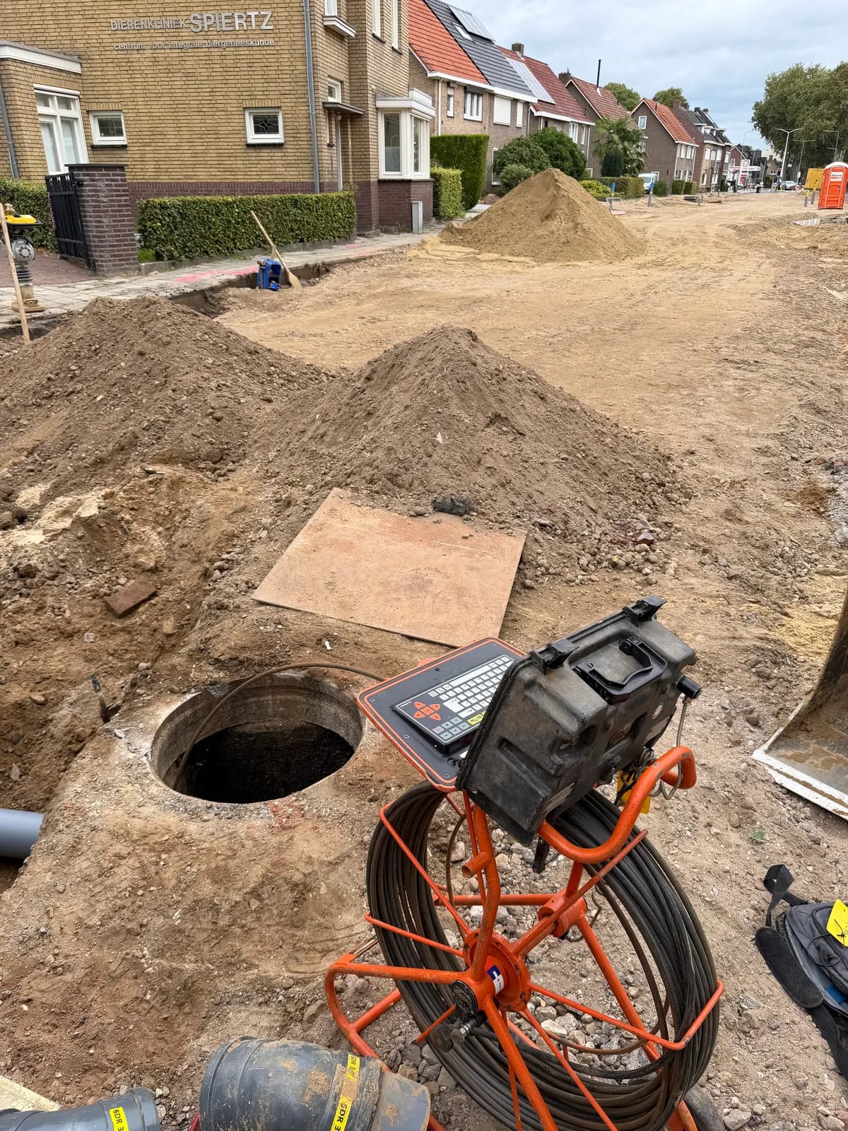 Rioolcamera met bedieningsunit naast een geopende inspectieput op een werkterrein