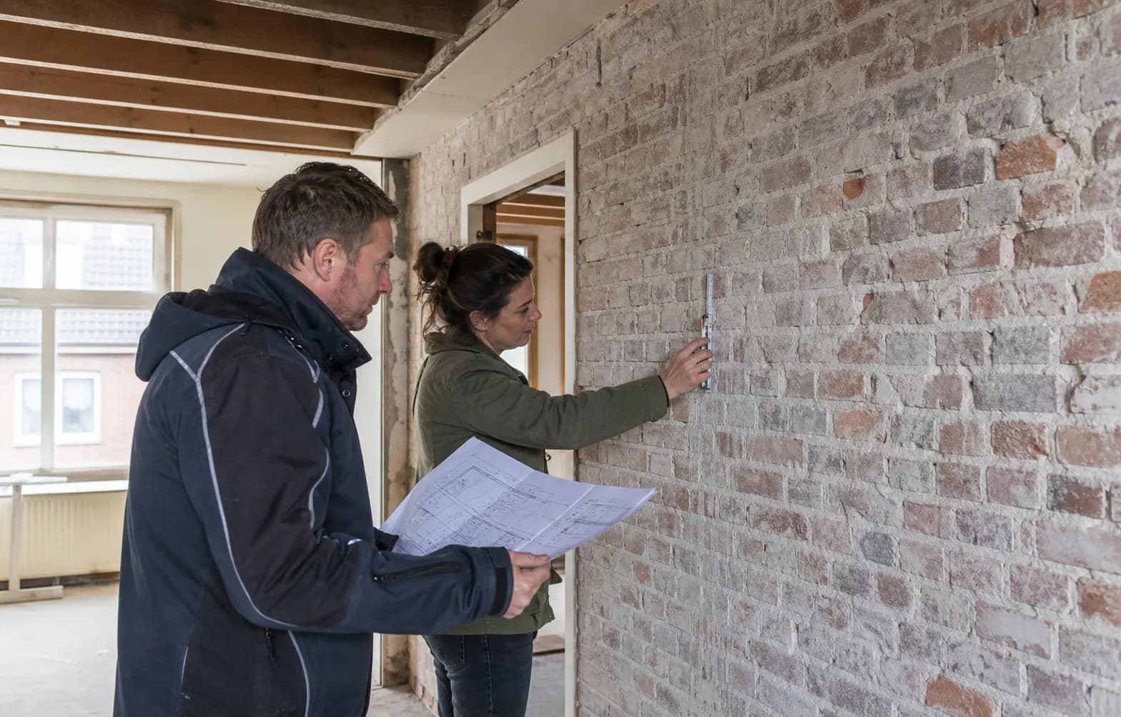 Nederlandse constructeur en aannemer beoordelen bouwtekeningen bij een gemarkeerde binnenmuur
