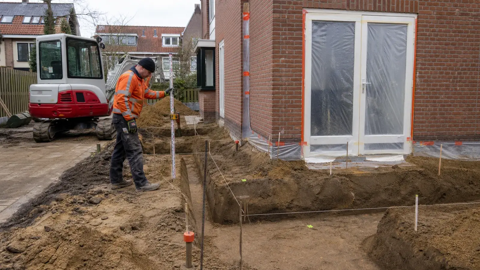 Compacte graafmachine graaft funderingssleuven voor een aanbouw aan een Nederlandse woning