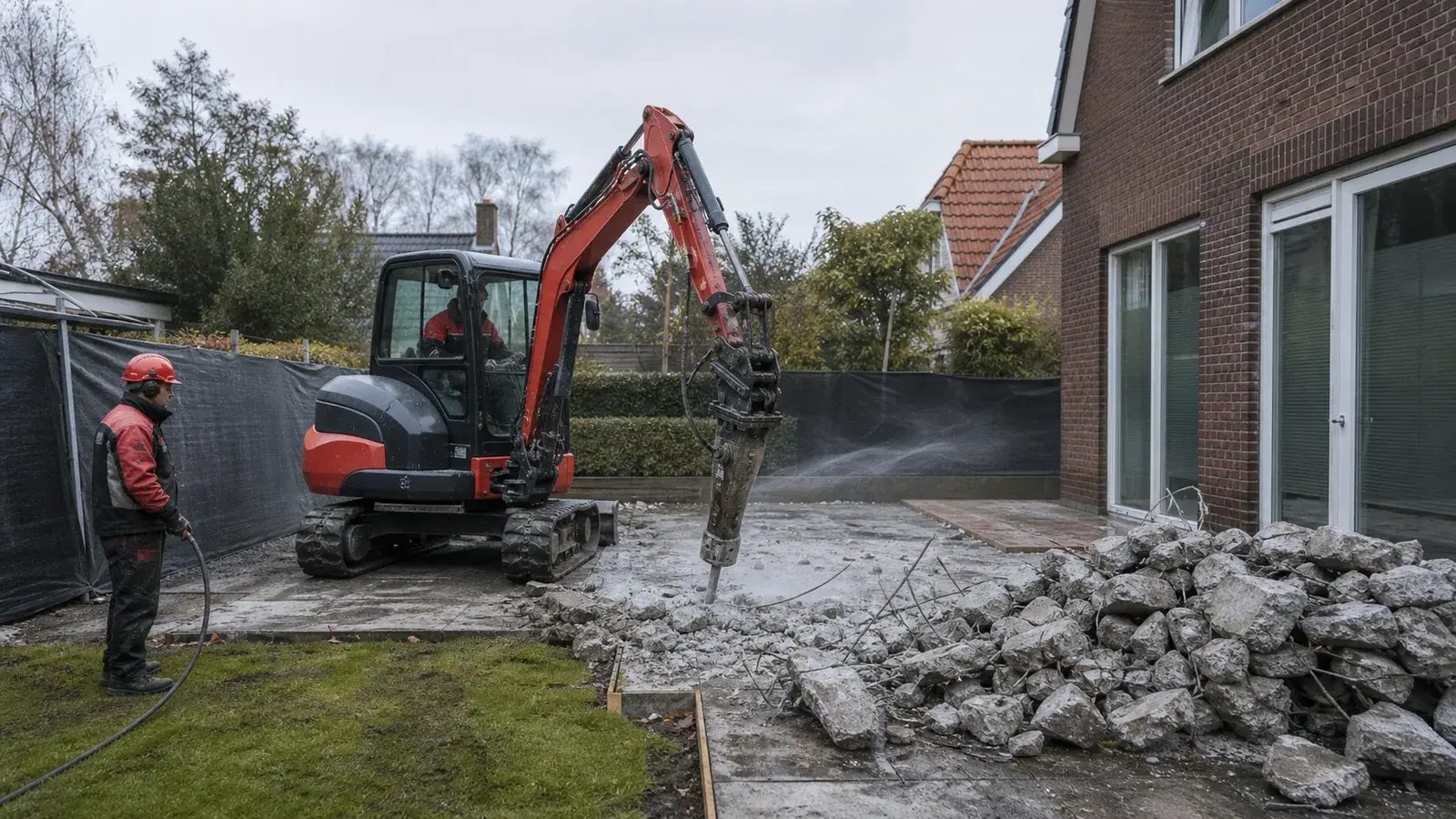 Compacte graafmachine breekt een betonnen terras uit bij een Nederlandse woning